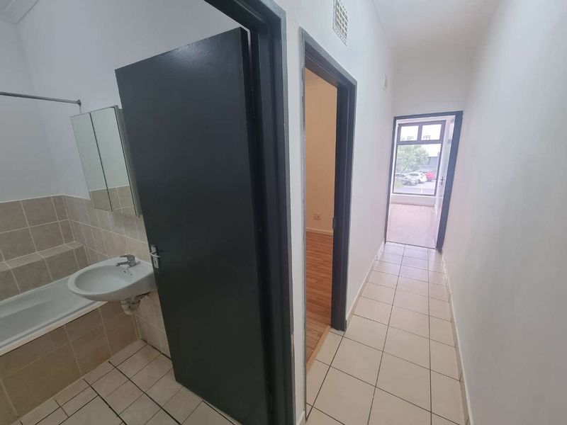 A functional hallway connecting to a bathroom area with a built-in bathtub and basin, featuring tiled flooring throughout.