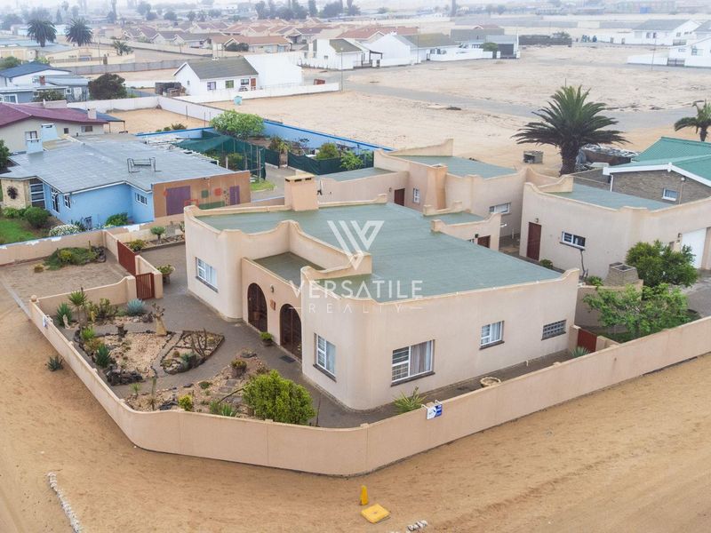 Aerial view of a single-story residential property featuring a flat roof, perimeter wall, and a paved courtyard area in a coastal setting.