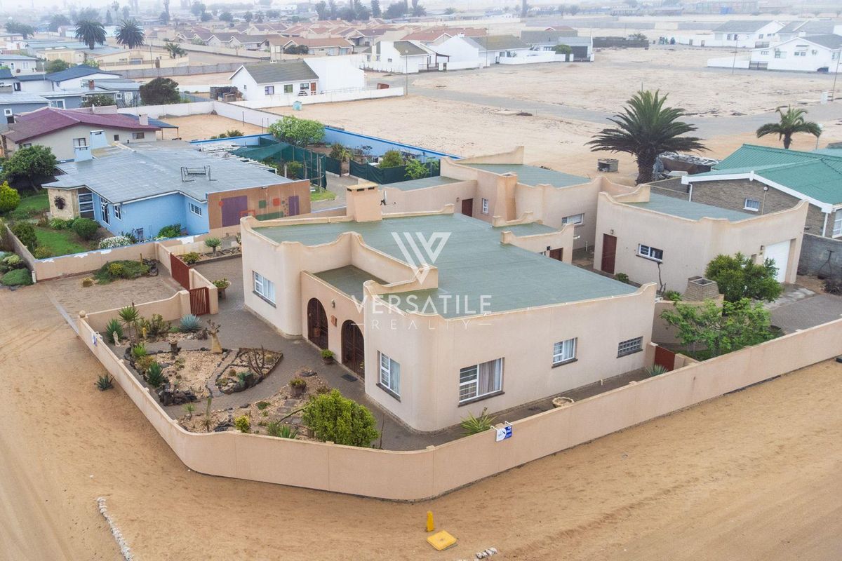 Aerial view of a single-story residential property featuring a flat roof, perimeter wall, and a paved courtyard area in a coastal setting.