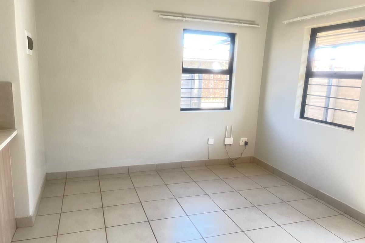 A clean, empty bedroom featuring neutral tiled flooring, large windows with security bars, and simple wall finishes, ready for personalization.