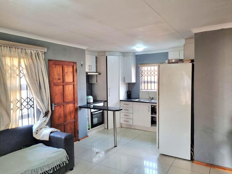Open-plan kitchen featuring built-in cabinetry, integrated oven, extractor fan, and a breakfast bar, seamlessly connected to the living area with tiled flooring.