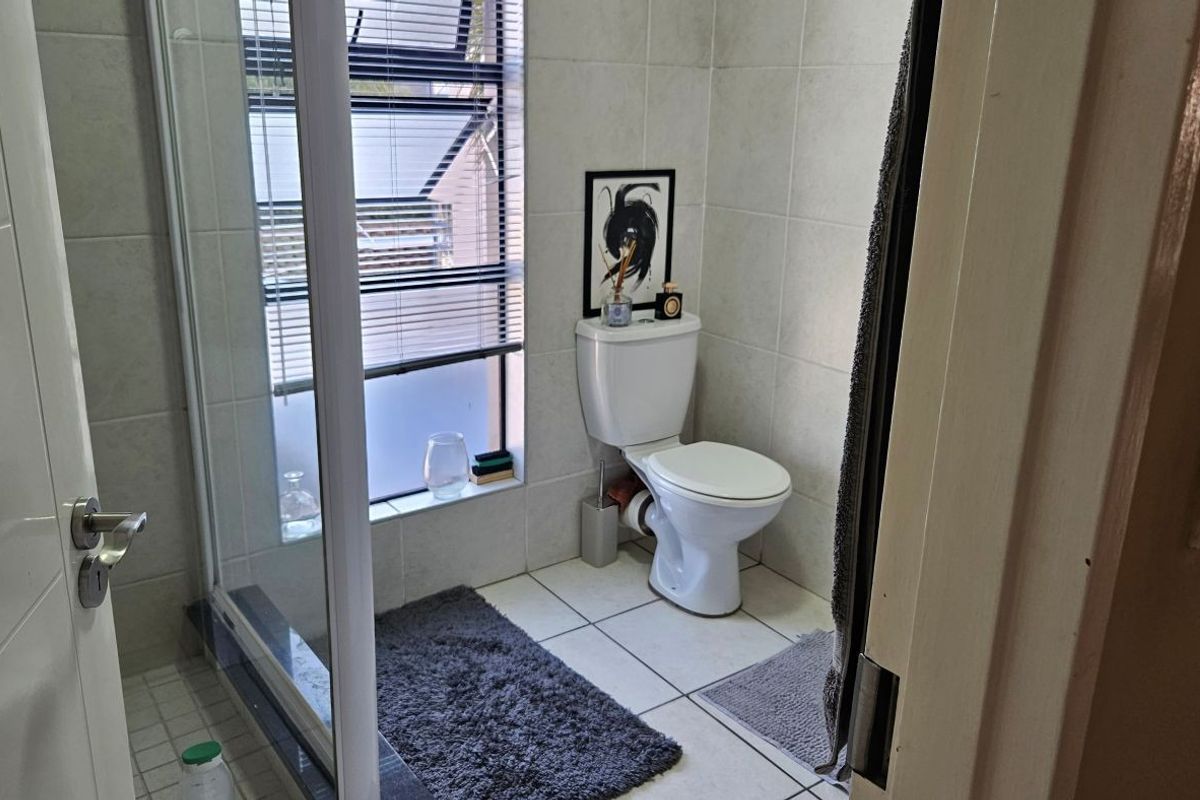 A functional bathroom featuring a shower enclosure, toilet, and neutral wall and floor tiling.