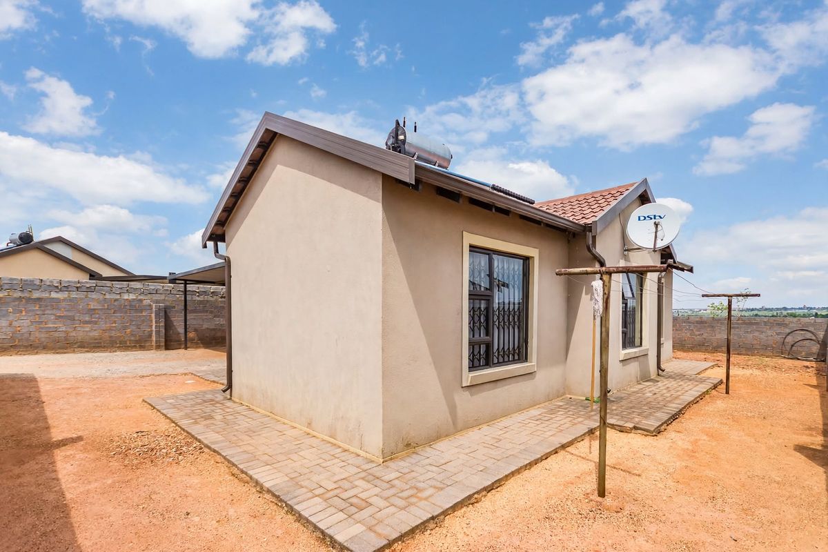 Rear view of the property featuring a paved walkway, solar water heating system, and secure window bars set within a fenced yard.
