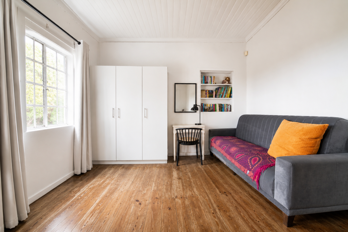 A bright bedroom featuring polished timber flooring, a built-in wardrobe, recessed shelving, and a classic beadboard ceiling with a steel-framed window.