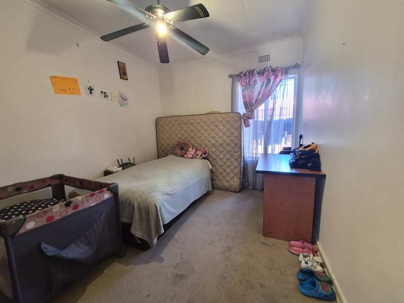 A bedroom featuring a ceiling fan, carpeted flooring, and a window with natural light, requiring cosmetic updates to improve its overall condition.