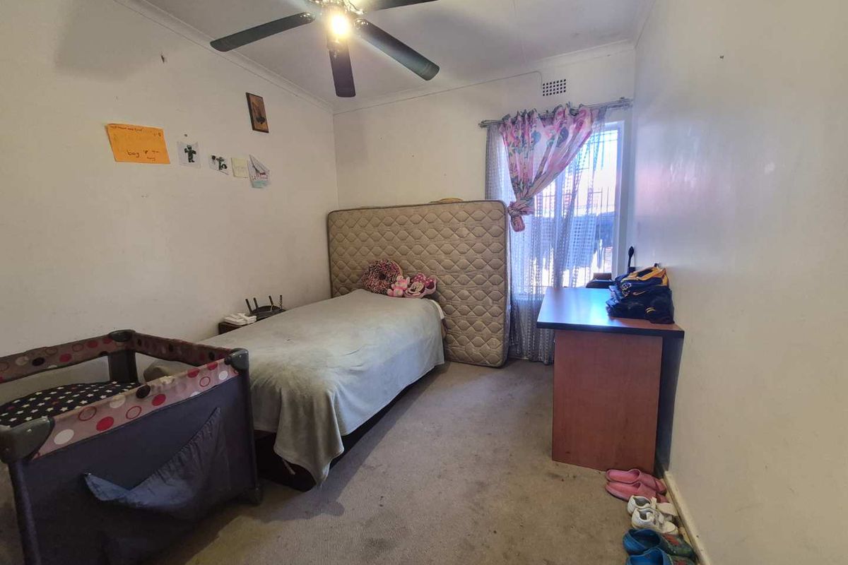 A bedroom featuring a ceiling fan, carpeted flooring, and a window with natural light, requiring cosmetic updates to improve its overall condition.
