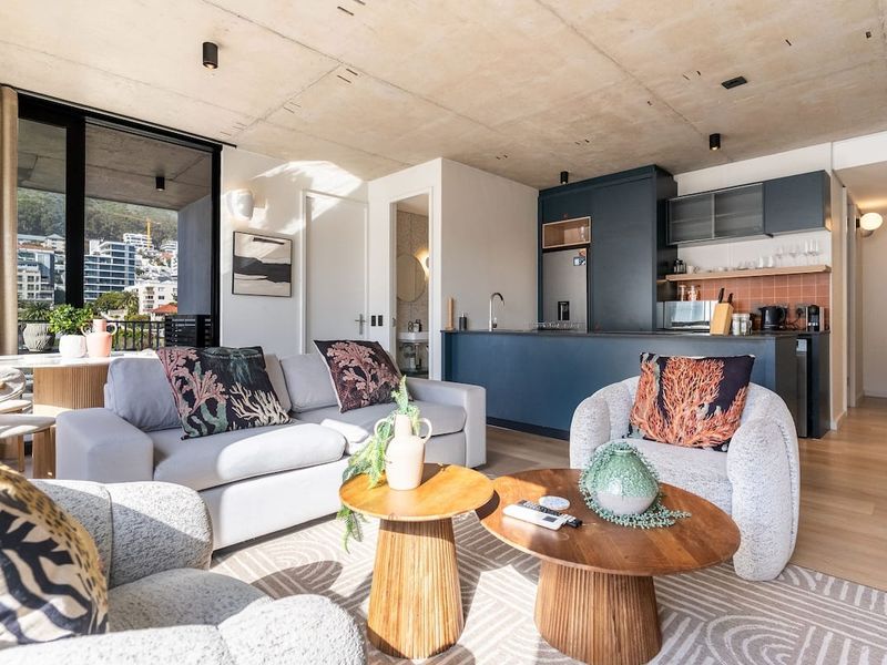 Modern open-plan living area featuring an exposed concrete ceiling, sleek kitchen cabinetry, and seamless access to a private balcony with urban views.