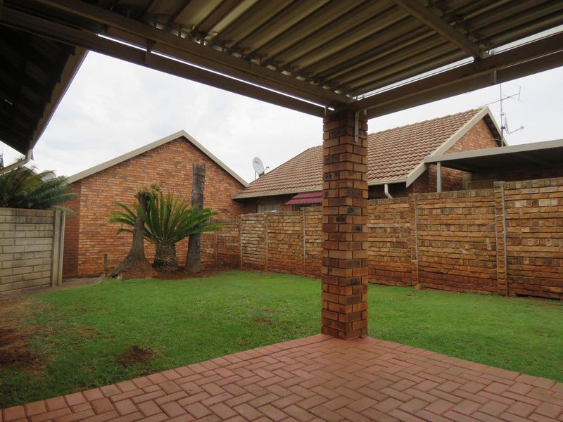 A covered patio area with brick paving and a brick support pillar, overlooking a private garden with a brick boundary wall.