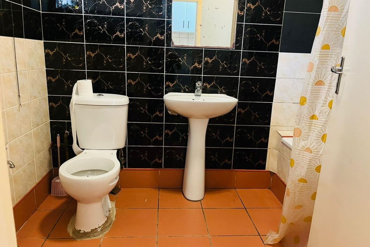 A functional bathroom featuring a pedestal basin, toilet, and bathtub with contrasting black and beige wall tiling and terracotta floor tiles.