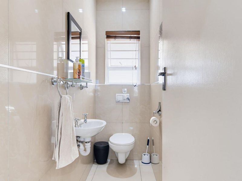 A compact, modern bathroom featuring wall-mounted sanitary ware, neutral floor-to-ceiling tiling, and a window for natural light.