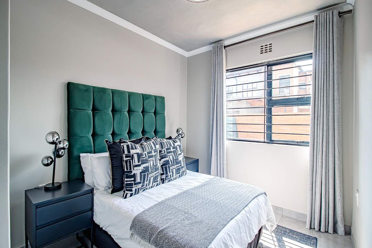 A well-maintained bedroom featuring neutral wall tones, tiled flooring, and a window fitted with security bars and curtain tracks.