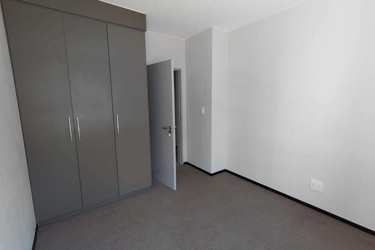 A clean, empty bedroom featuring neutral grey built-in cupboards, carpeted flooring, and a simple, modern aesthetic ready for personalization.