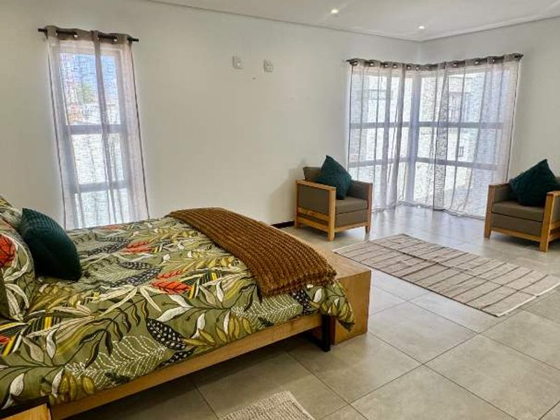 Spacious bedroom featuring large windows, neutral tiled flooring, and recessed downlighting, offering a bright and comfortable living space.