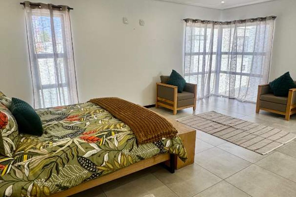 Spacious bedroom featuring large windows, neutral tiled flooring, and recessed downlighting, offering a bright and comfortable living space.