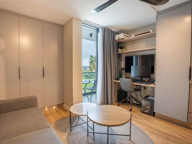 Modern bedroom featuring built-in cupboards, a dedicated desk area, ceiling fan, and direct access to a private balcony through sliding glass doors.