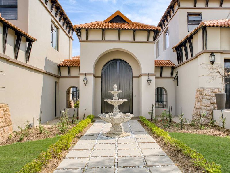 A grand front entrance featuring a symmetrical facade, terracotta roof tiles, stone accents, and a central stone fountain leading to a large arched doorway.