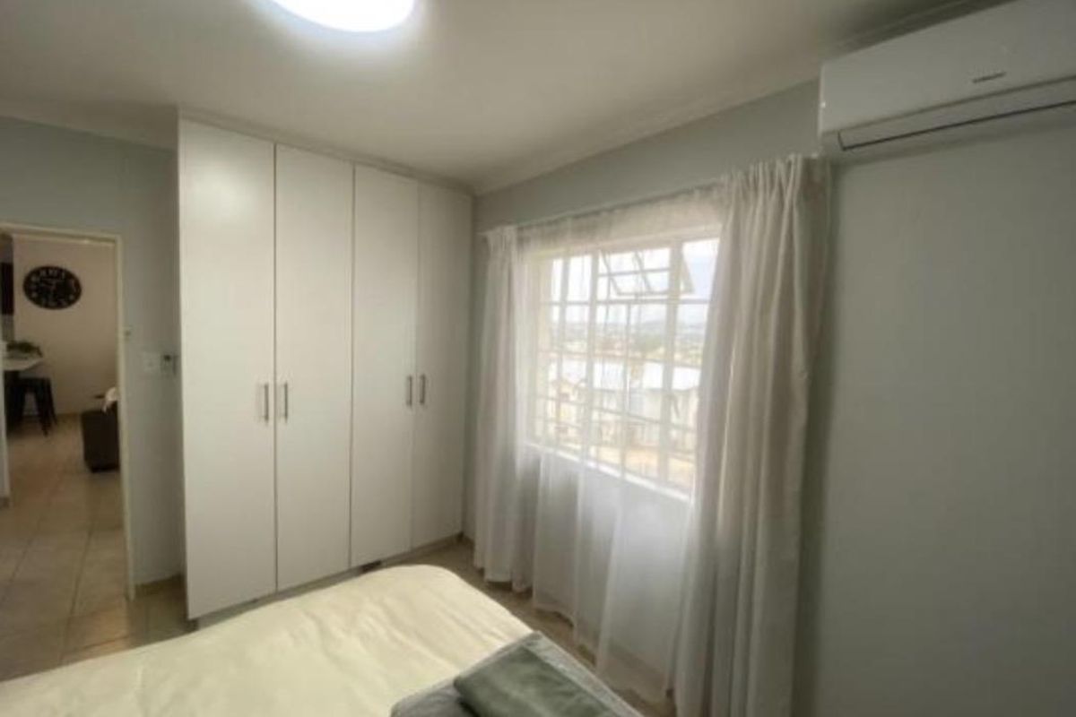 A bright bedroom featuring built-in floor-to-ceiling wardrobes, a wall-mounted air conditioning unit, and a window with security bars.