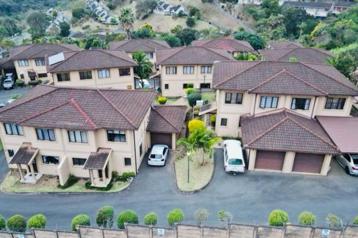 Aerial view of a townhouse complex featuring multiple units with tiled roofs, private garages, and paved driveway access within a landscaped estate setting.