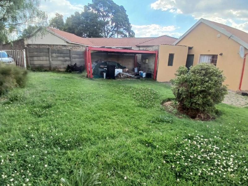Rear garden view featuring a lawn, precast boundary wall, and a covered carport structure attached to the main house.