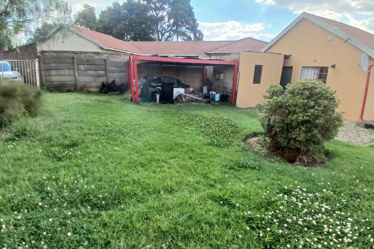 Rear garden view featuring a lawn, precast boundary wall, and a covered carport structure attached to the main house.