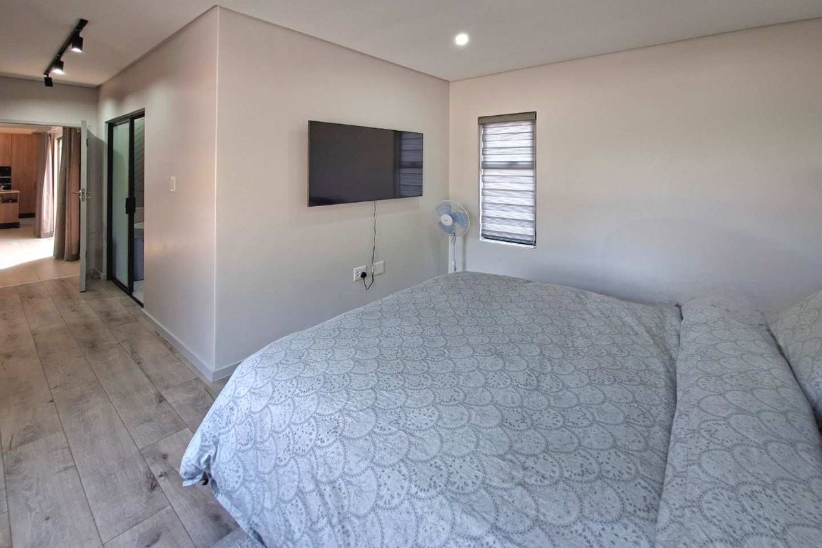A well-maintained bedroom featuring modern laminate flooring, recessed downlighting, and a neutral color palette, with direct access to an adjacent room.