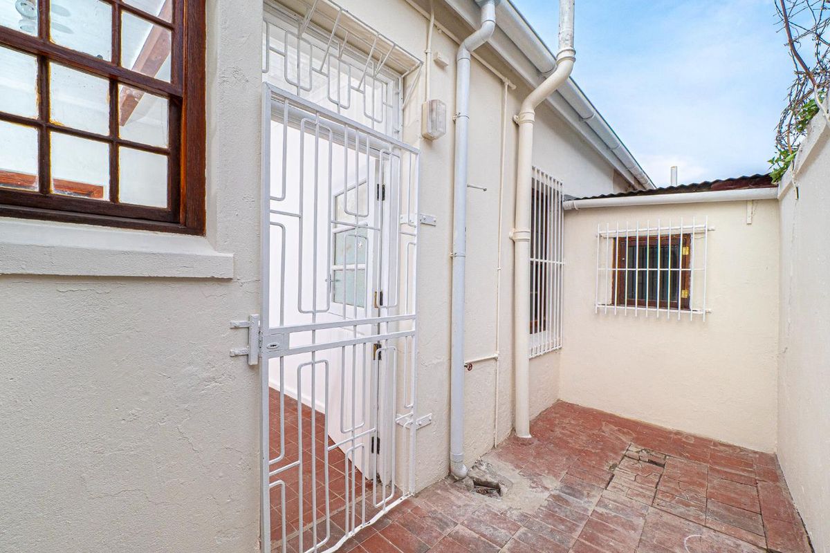 A rear exterior courtyard area featuring terracotta paving, security gates, and security bars on the windows.