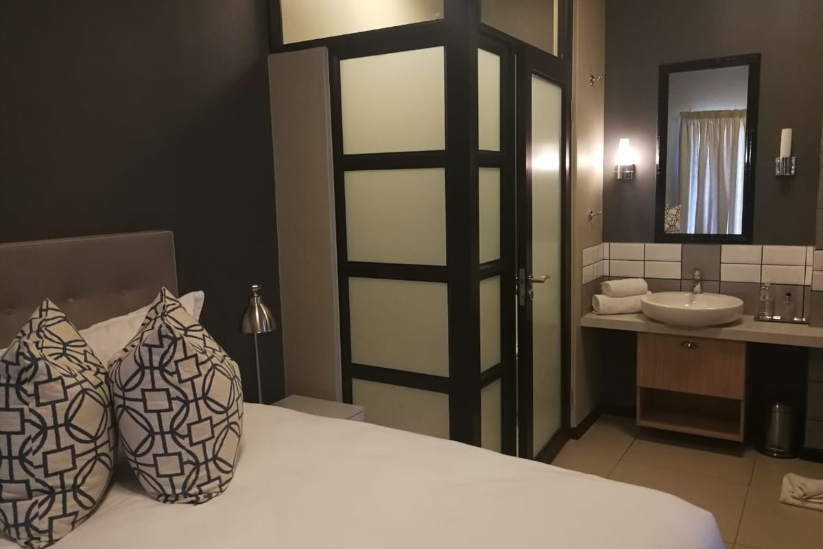 A modern bedroom featuring an integrated en-suite bathroom with a frosted glass partition, vessel sink, and vanity cabinet.