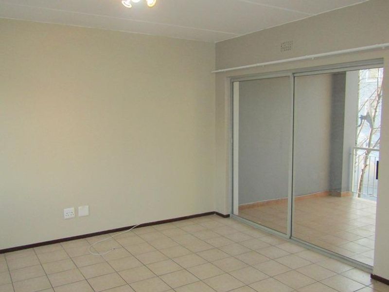 An empty living room featuring neutral walls, tiled flooring, and a large sliding glass door providing access to an outdoor balcony area.