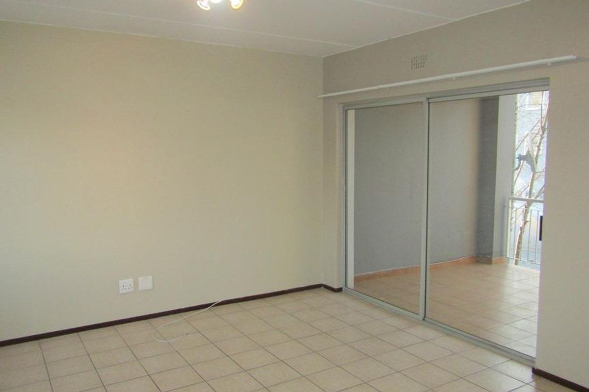 An empty living room featuring neutral walls, tiled flooring, and a large sliding glass door providing access to an outdoor balcony area.