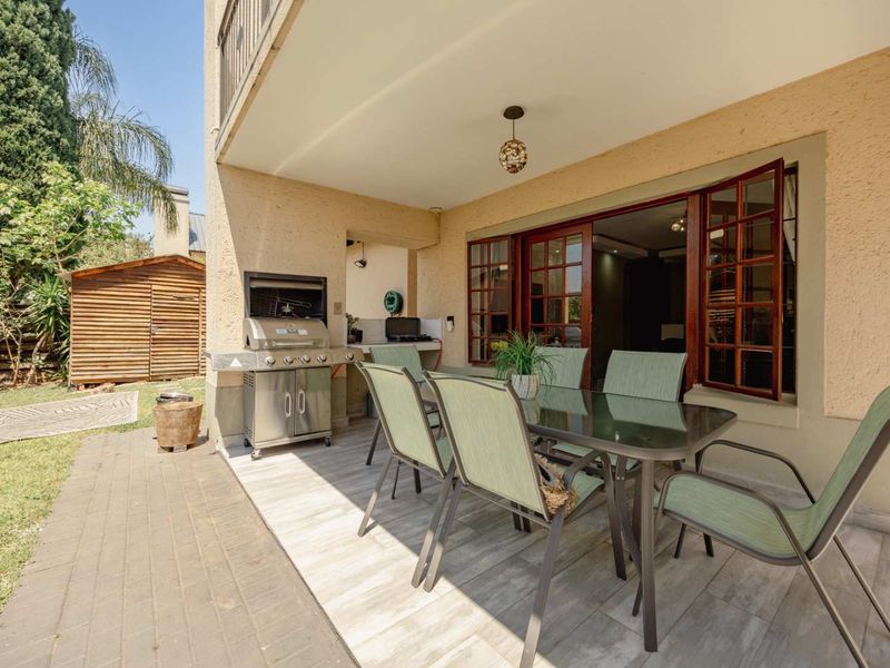 Covered patio area featuring a built-in braai, tiled flooring, and direct access to the interior through timber frame doors.