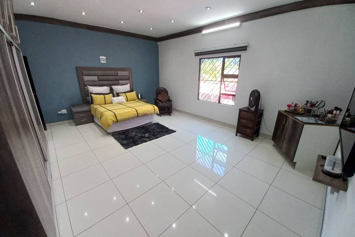 Spacious bedroom featuring large format floor tiles, recessed downlighting, and a feature wall, providing a clean and modern living space.