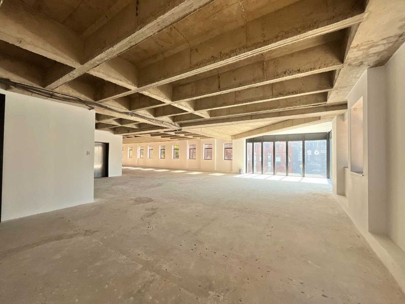Spacious open-plan office area featuring an exposed concrete waffle ceiling, large windows providing natural light, and an unfinished floor ready for custom fit-out.