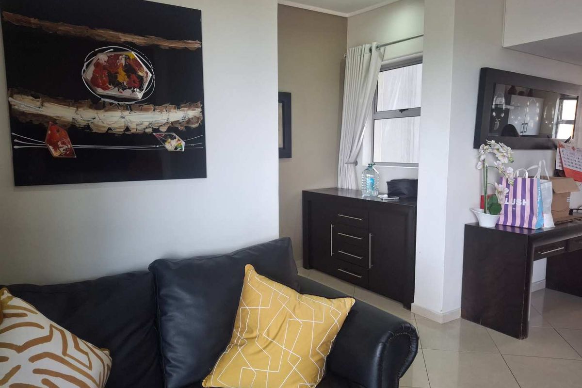 A living room area featuring tiled flooring, recessed ceiling lights, and an aluminium window frame, providing a functional and neutral living space.
