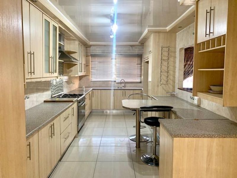 A functional kitchen featuring light wood-finish cabinetry, stone-look laminate countertops, a built-in gas hob, oven, and a convenient breakfast bar area.