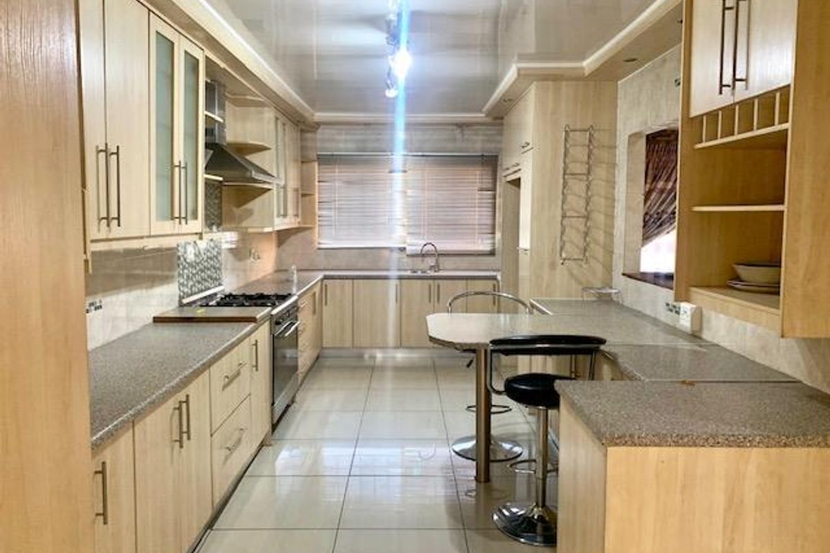 A functional kitchen featuring light wood-finish cabinetry, stone-look laminate countertops, a built-in gas hob, oven, and a convenient breakfast bar area.