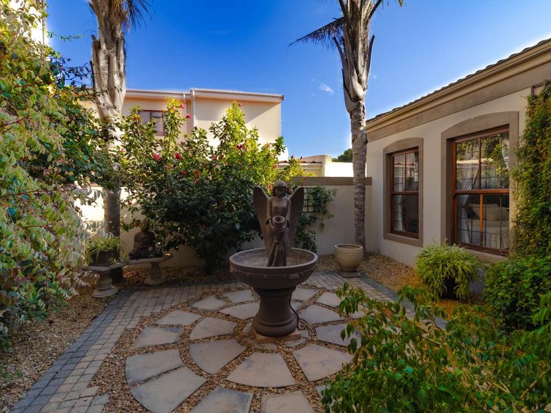 A tranquil courtyard garden featuring a central stone fountain, paved circular patio area, and established landscaping enclosed by boundary walls.