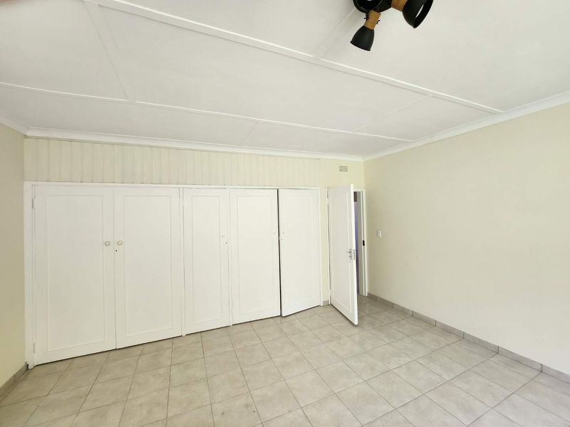 A spacious, empty bedroom featuring neutral tiled flooring, built-in cupboards, and a ceiling fan, offering a clean canvas for personalization.