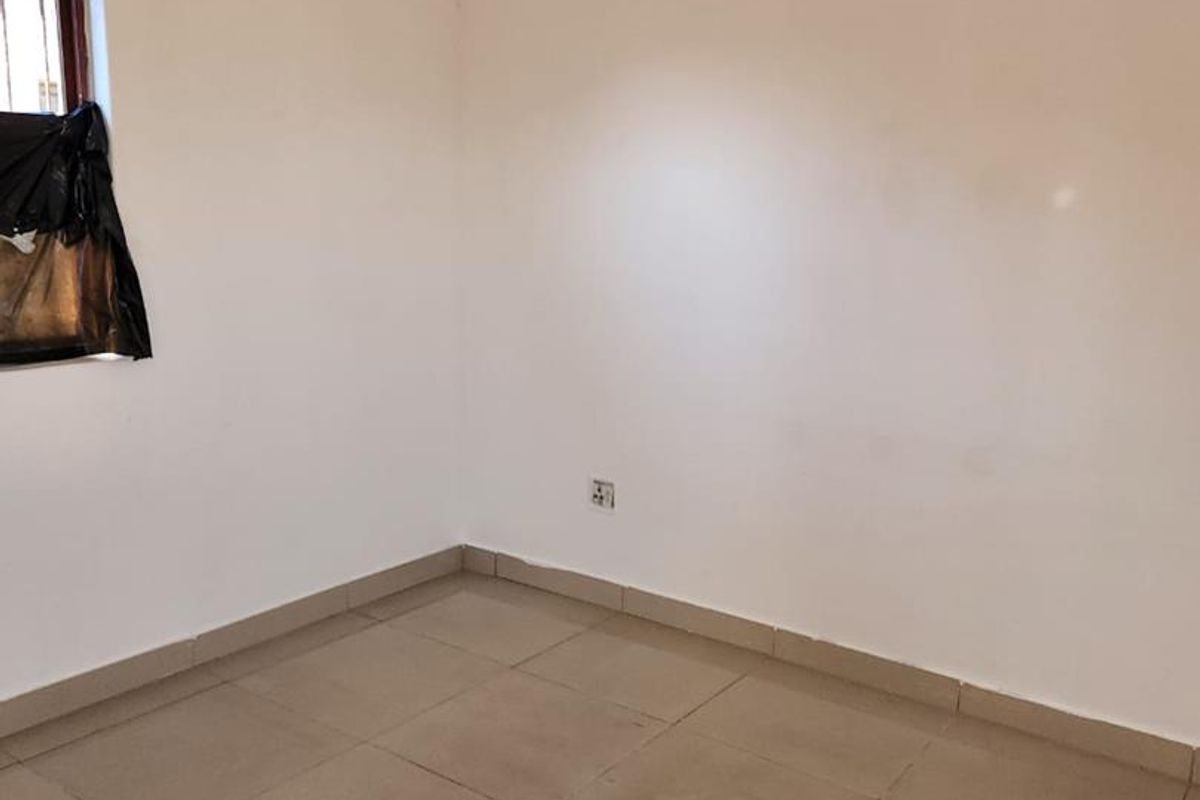 A simple, empty bedroom featuring neutral tiled flooring and plain white walls, offering a blank canvas for personalization.