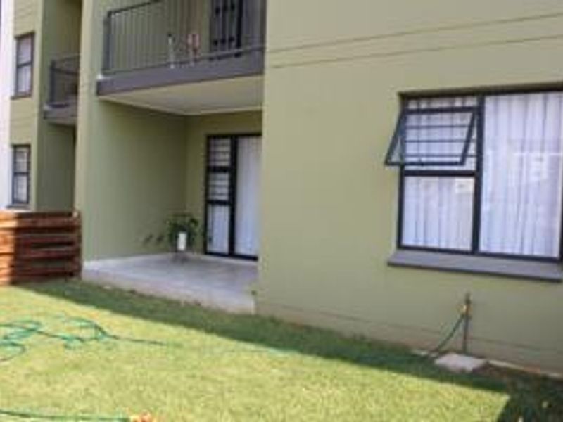 Rear view of the apartment featuring a ground floor patio, a first-floor balcony with metal railing, and a small private garden area.