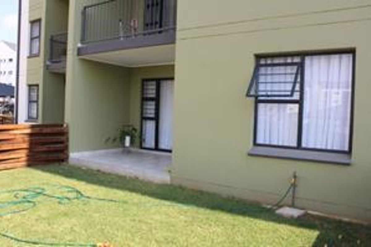Rear view of the apartment featuring a ground floor patio, a first-floor balcony with metal railing, and a small private garden area.