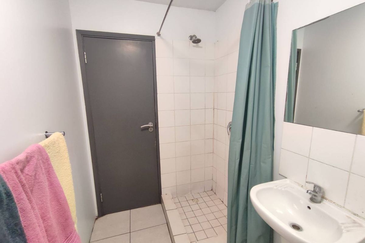 A functional bathroom featuring a tiled shower enclosure, wall-mounted basin, and mirror, providing essential amenities in a compact layout.