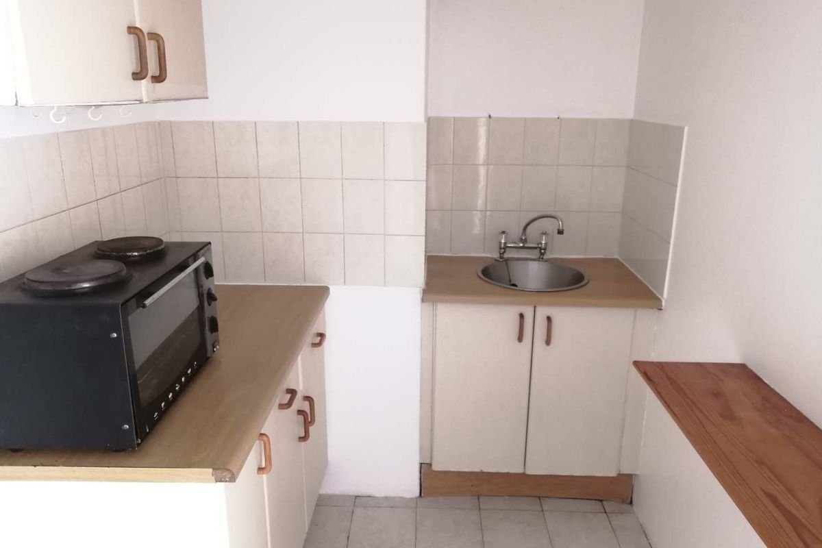 Compact kitchen featuring basic cabinetry, a stainless steel sink, tiled splashback, and a small countertop area.