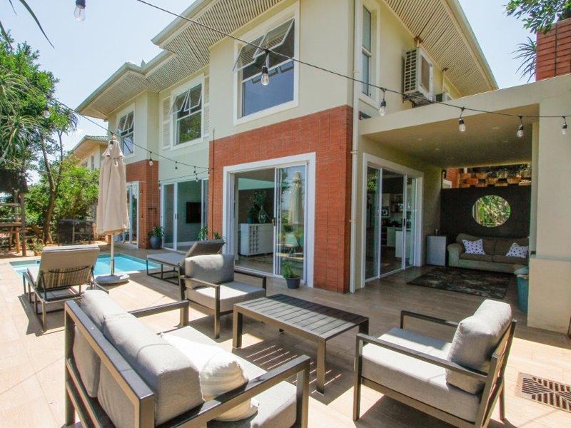 Rear exterior view of the townhouse featuring a covered patio, tiled outdoor area, and a swimming pool with brick and plaster facade.