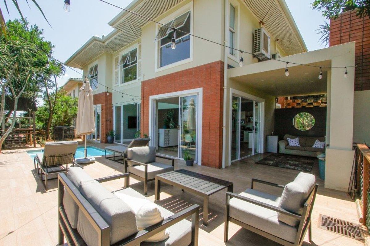Rear exterior view of the townhouse featuring a covered patio, tiled outdoor area, and a swimming pool with brick and plaster facade.