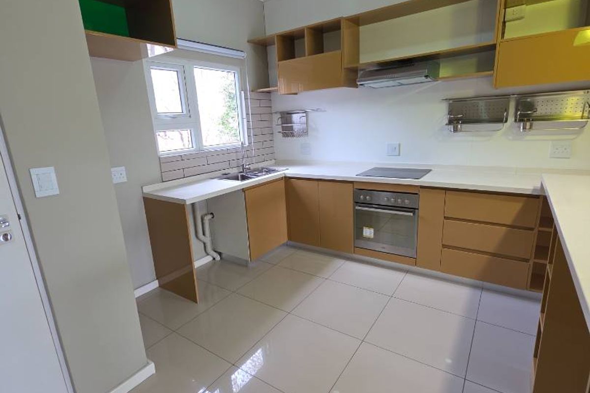 Modern kitchen featuring light wood cabinetry, white countertops, built-in oven, extractor fan, and tiled flooring with recessed ceiling lighting.