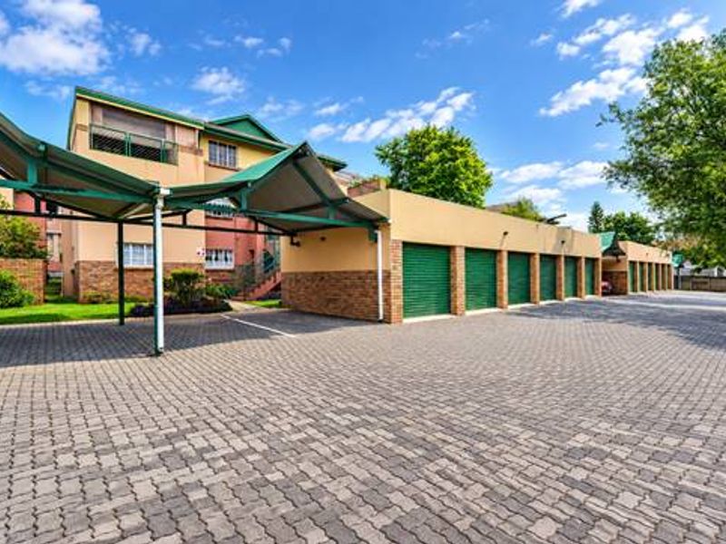 Exterior view of the townhouse complex featuring a paved driveway, covered carport parking, and a row of secure lock-up garages.