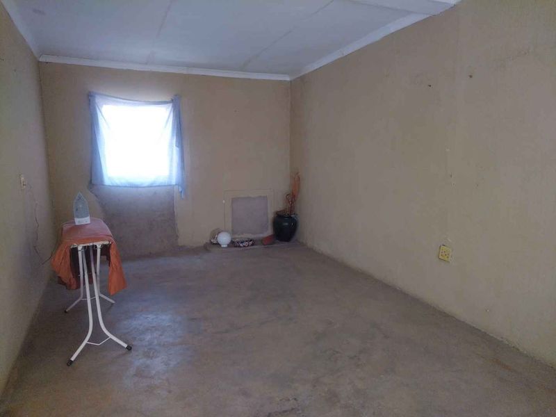 A basic, unfinished bedroom space featuring plain walls, a single window, and concrete flooring, offering a blank canvas for renovation.