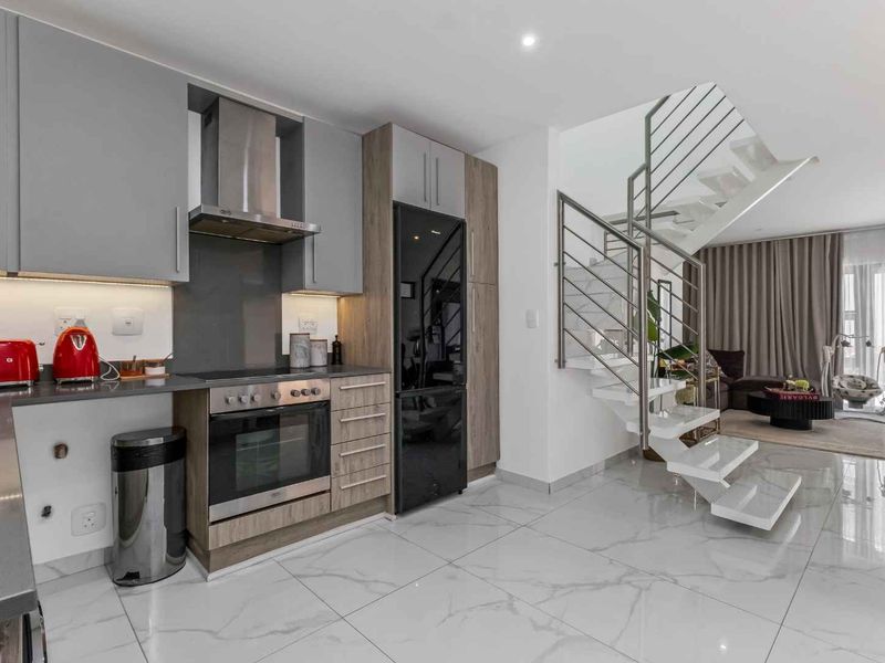 Modern open-plan kitchen featuring sleek grey and wood-tone cabinetry, integrated appliances, and a striking staircase with a contemporary metal railing.