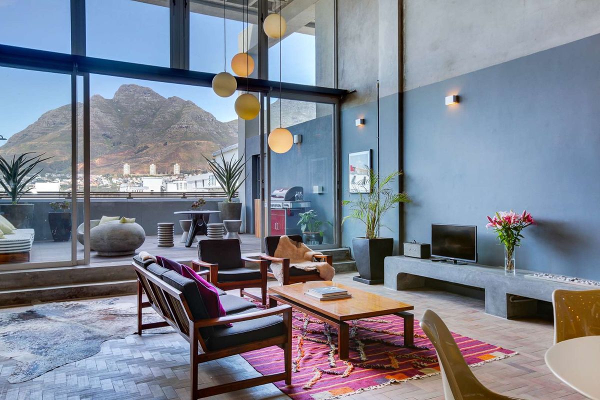 Spacious living area featuring high ceilings, herringbone timber flooring, and floor-to-ceiling glass doors opening onto a private balcony with mountain views.