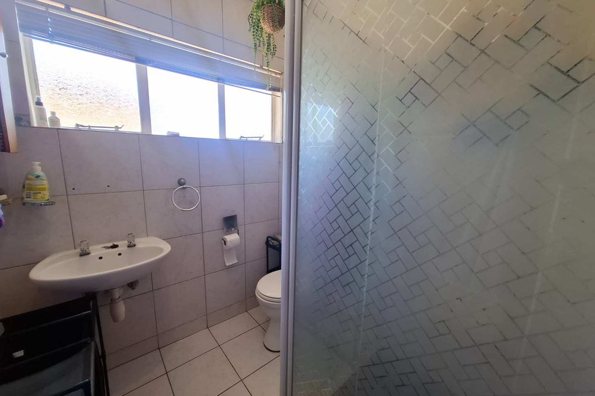 A functional bathroom featuring a shower enclosure, pedestal basin, and toilet with neutral wall and floor tiling.
